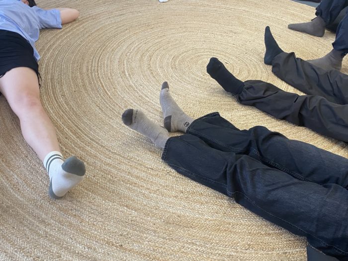 A close up of the legs of 4 people lying on the floor over a straw rug