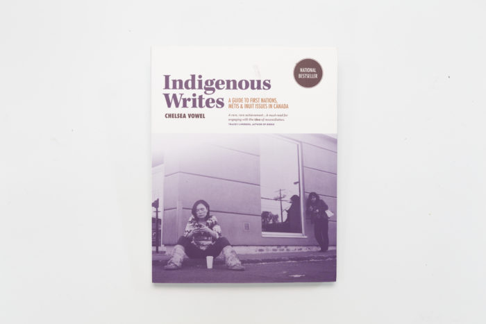 The cover of the book "Indigenous Writes" with a purple tainted image of two people in the street, one sitting in the floor at the front and another in the back standing up. Both of them are looking at their phones. 